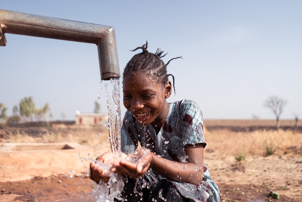 Happy,Little,African,Girl,Crouching,In,Front,Of,A,Waterhole